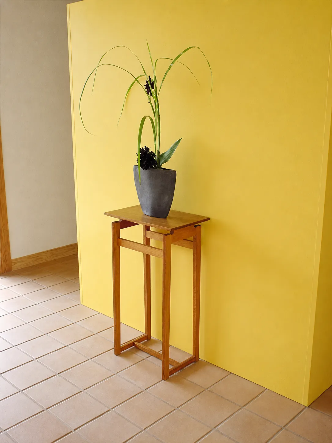 黄色い壁のそばに置かれたフラワーテーブル。鉢植えの花が飾られている。